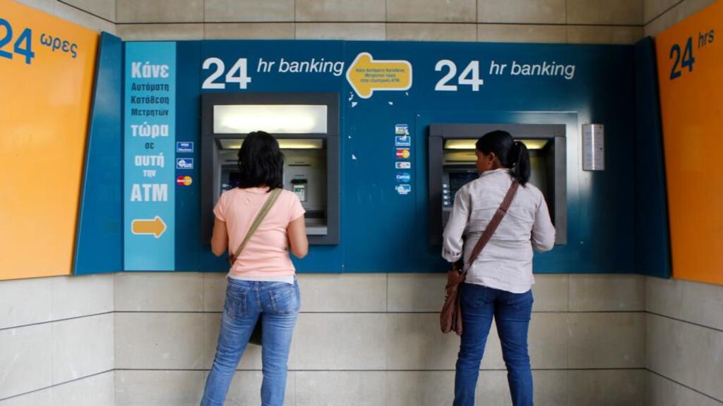 Women withdraw money from ATMs at a branch of the Bank of Cyprus at Eleftheria square in Nicosia late last month. Major depositors in Cyprus's biggest bank will lose around 60 percent of savings over €100,000, its central bank confirmed on Saturday.