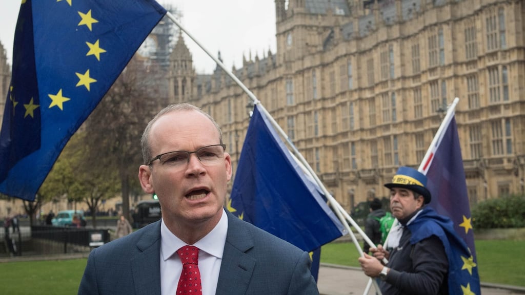 A man holding EU flags walks behind Minister for  Foreign Affairs  Simon Coveney as he speaks to the media on College Green in Westminster, London, on Friday  after talks with newly appointed Northern Ireland Secretary Karen Bradley. Photograph: PA