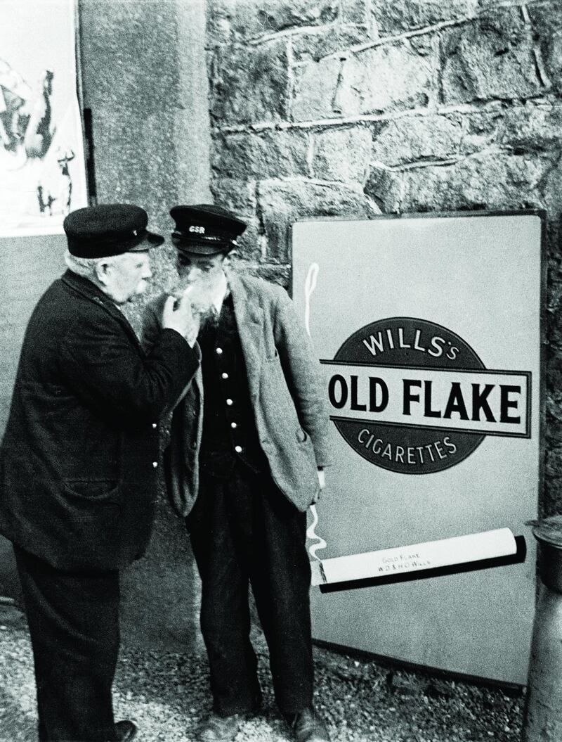 An image from 1933 of railway workers lighting cigarettes beside an advertisement for the product at Wicklow station draws comparisons with humanist photographers Henri Cartier-Bresson and Robert Doisneau
