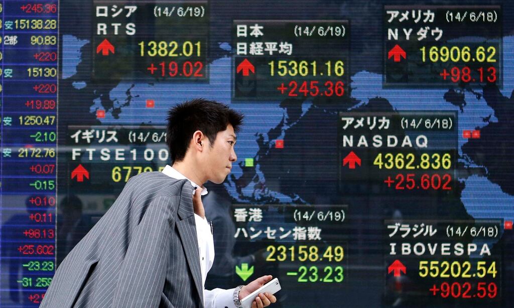 A pedestrian holding his mobile phone walks past an electronic board showing the stock market indices of various countries outside a brokerage in Tokyo.