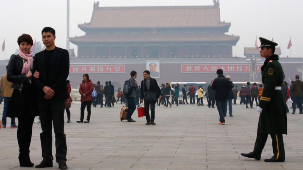 A paramilitary soldier patrols near visitors posing for souvenir pictures at Tiananmen Square in Beijing