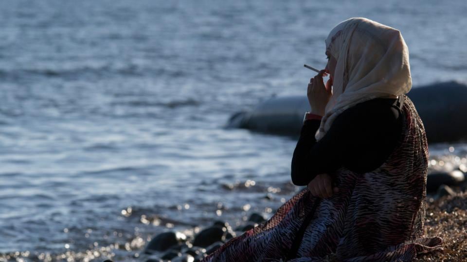 A Syrian refugee on Lesvos on Tuesday. The remains of the inflatable boat on which had arrived the previous day can be seen in the background. Photograph: Nikolas Georgiou