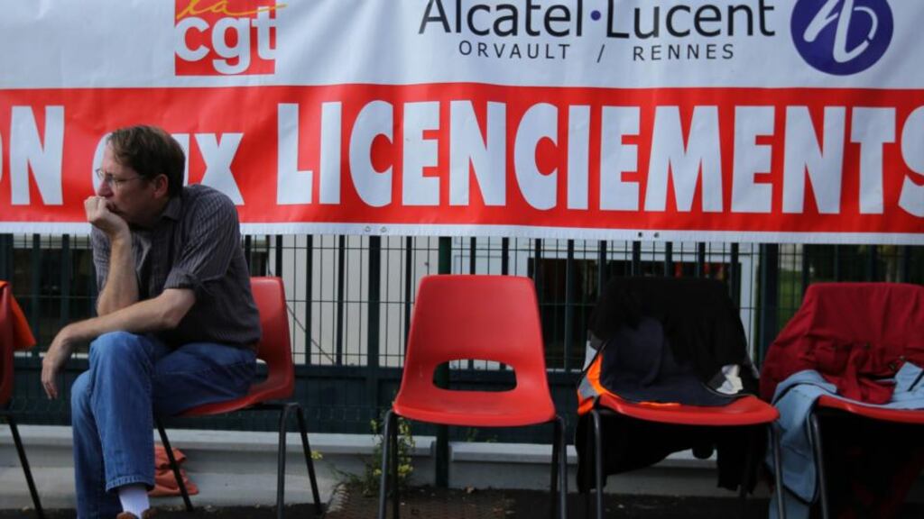 An employee of Alcatel-Lucent sits in front of a banner which reads “no layoffs” during a demonstration at the company site in Orvault near Nantes,  France, yesterday. Photograph:  Reuters/Stephane Mahe
