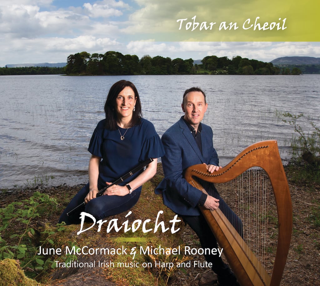 June McCormack holds her flute beside Michael Rooney with his harp, both sitting beside a lake
