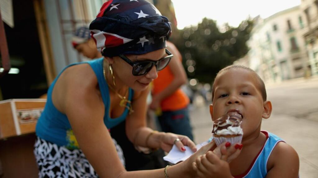 The United States flag is appearing in small ways in the clothing worn by Cubans, like the scarf worn by Gydis Ricardo Vargas as she gives her son Wisin Abascal Ricardo some ice cream in Havana, Cuba. Photograph: Chip Somodevilla/Getty Image