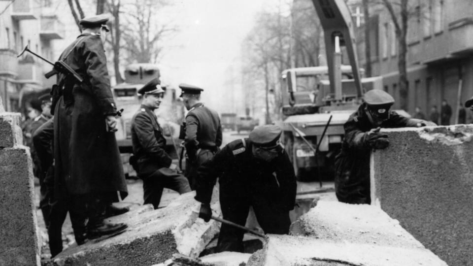 Officers inspecting the damage to the Berlin Wall, East Germany, and making preparations for its repair, after an East German rammed the Wall with an army car and successfully escaped