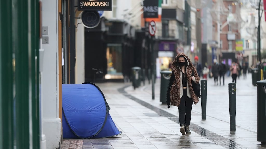 A woman walks past the tent of a homeless person on Grafton Street in Dublin during lockdown. Photograph: Niall Carson/PA Wire