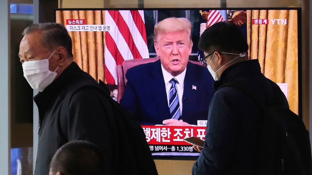 Masked people walk in front of a TV screen showing a live broadcast of US president Donald Trump’s speech.