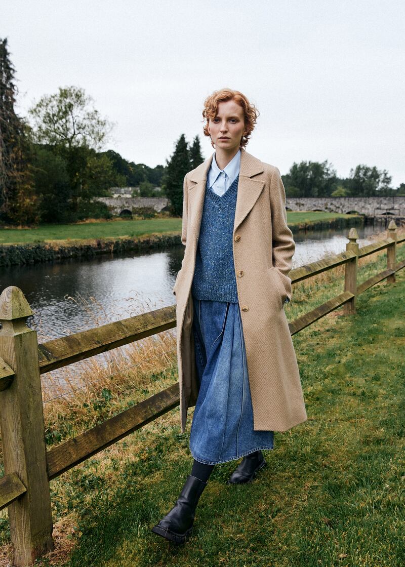 Camel herringbone merino and cashmere blend belted coat, €699, Triona; blue tweed knit vest, €107, Fisherman out of Ireland; blue cotton shirt, €270, Eudon Choi; denim pleated skirt, €360, Tela, both at Beautiful South, Rathmines