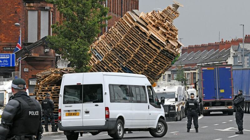 The Cluan Place bonfire in east Belfast is knocked over by a fork lift vehicle as police guard masked contractors removing wooden pallets and tyres from the site after it was decided that the structure was too high.