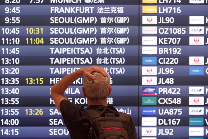 A traveller stands in front of a flight information board at Haneda International Airport in Tokyo. Photograph: Eugene Hoshiko/AP