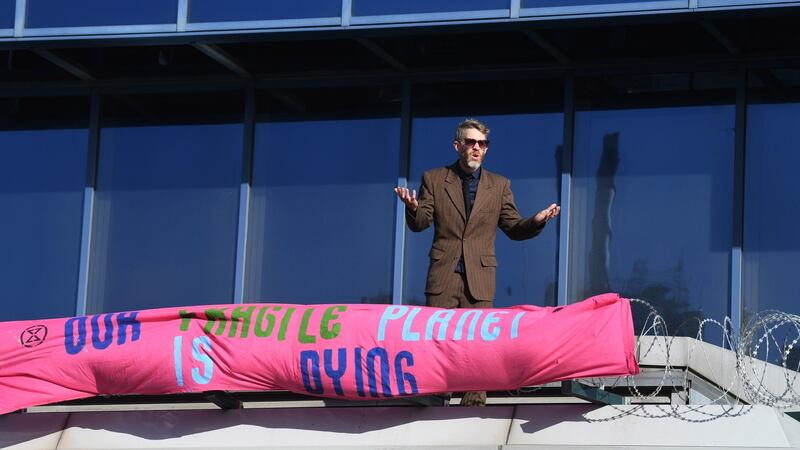An Extinction Rebellion protester stands on the airport roof as they try to blockade London City Airport. Photograph. Facundo Arrizabalaga/EPA