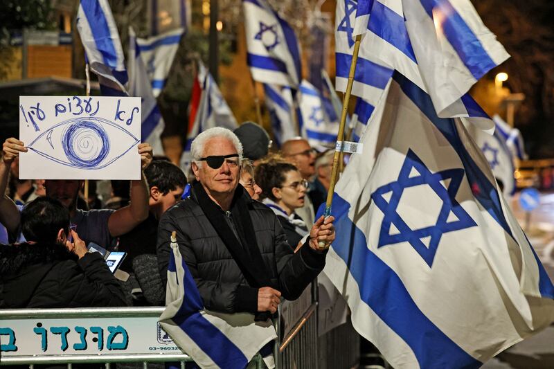 Protester waves Israeli flag while another holds a sign reading in Hebrew 'we won't close our eyes'. Photograph: Ahmad/Gharabali/AFP/Getty Images