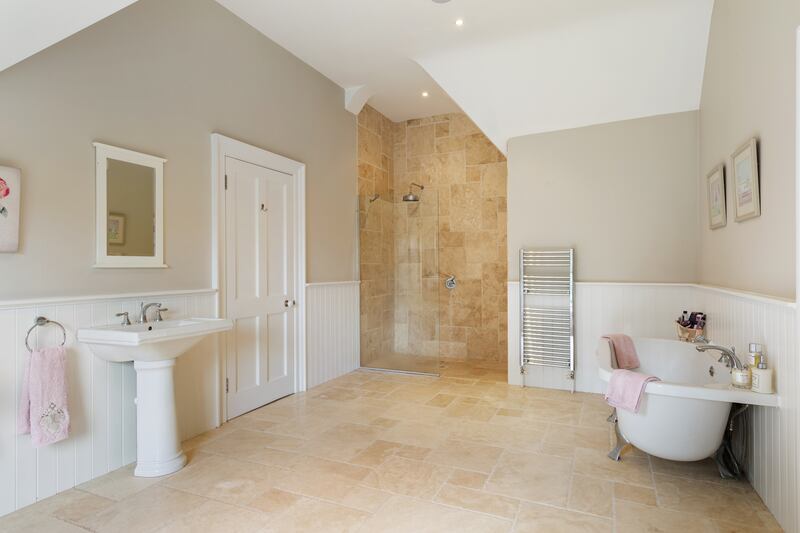 A big en suite has a rolltop bath, two sinks and a step-in shower tiled with natural stone.