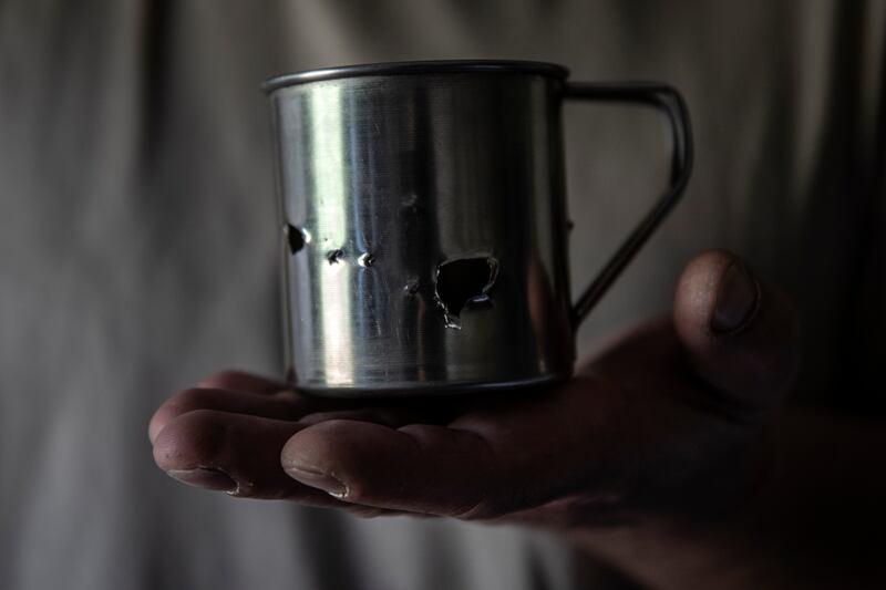 Samara, 48, holds his tin cup that was punctured with shrapnel holes after he left it outside the trench during a bombardment. 