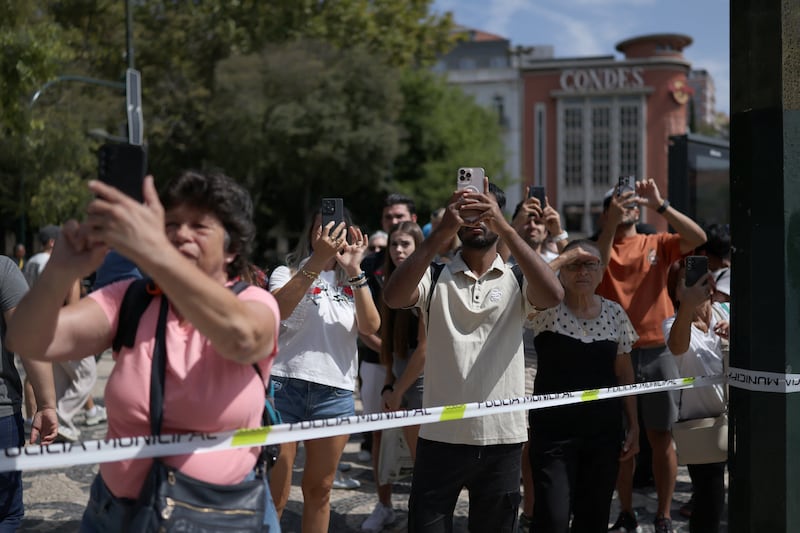 People behind a security cordon take pictures of the site of the Glória Funicular crash that left 17 people dead in Lisbon. Photograph:  Patricia de Melo Moreira/AFP via Getty Images)        