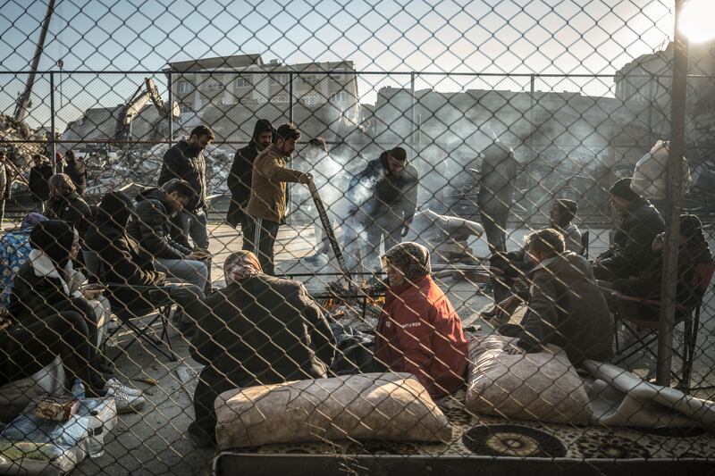 Earthquake survivors gather around a bonfire near collapsed buildings in Hatay, Turkey on Wednesday. Phortograph: Sergey Ponomarev/New York Times