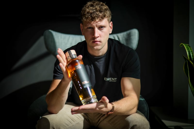 Fionn Cox, the co-founder of Element Irish Whiskey, standing while holding a bottle of the brand's whiskey