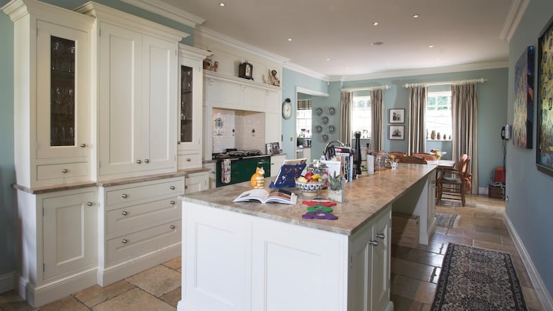 The L-shaped Dalkey Design kitchen/diningroom has a very large granite-topped island unit, a glossy green Aga set into the tiled chimneybreast, and smart cream timber units.
