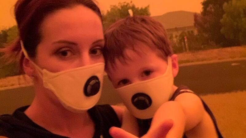 Amy Houghton and her son wearing masks stand under a sky tinted red as surrounding bushfires close in on the town of Mallacoota, Victoria. Photograph: Reuters