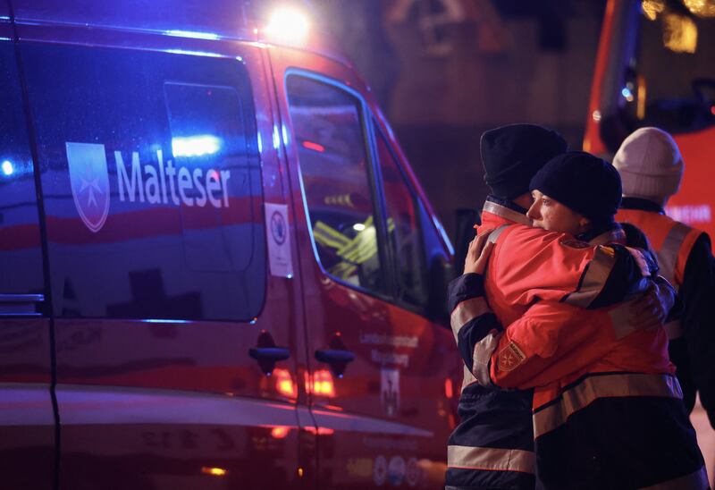 Rescuers hug next to the market after responding to the incident. Photograph: Ronny Hartmann/AFP via Getty Images