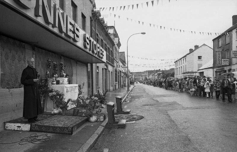 Seán Hillen: “I was entranced by this scene from the moment I saw it,  primarily because of the altar placed under the awning of a Dunnes Stores supermarket, the slightly Mediterranean enthusiasm (if under a grey and wet Irish sky) with the bunting, and the quite startling length of the parade, which is nearly the length of the town.”