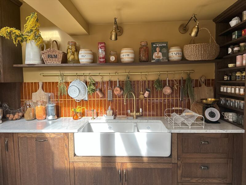 A brass rail under the shelving holds utensils and bunches of drying herbs