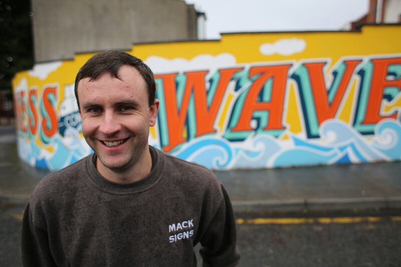 Cormac Dillon of Mack Signs, a traditional sign writer and mural artist, standing in front of a piece of street jointly created by him and 'Signs of Power' painter Vanessa Power near George’s Street in Dun Laoghaire. Photograph: Bryan O’Brien