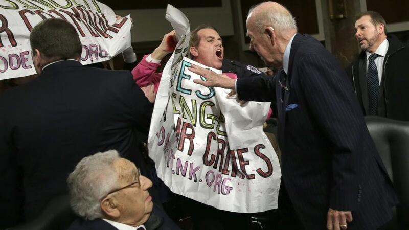Former US secretary of state George Shultz (R) pushes away protesters shouting “Arrest Henry Kissinger for war crimes” as Mr  Kissinger (L) watches on. Photograph: Win McNamee/Getty Images.