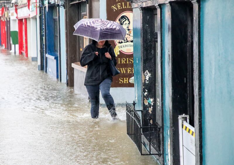 A woman wades through a flooded Main Street as she makes her way to work in Carrigaline, Co Cork. Photograph: David Creedon
