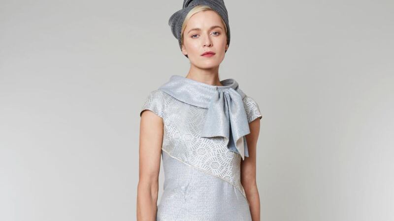 Mink: Knee-length tailored dress in Lurex threaded ice blue wool with gilded lace on bodice and sleeves. It has an asymmetrical style empire line and optional bow collar. It can be made with three-quarter length or full-length sleeves as required. Approx €1,320.