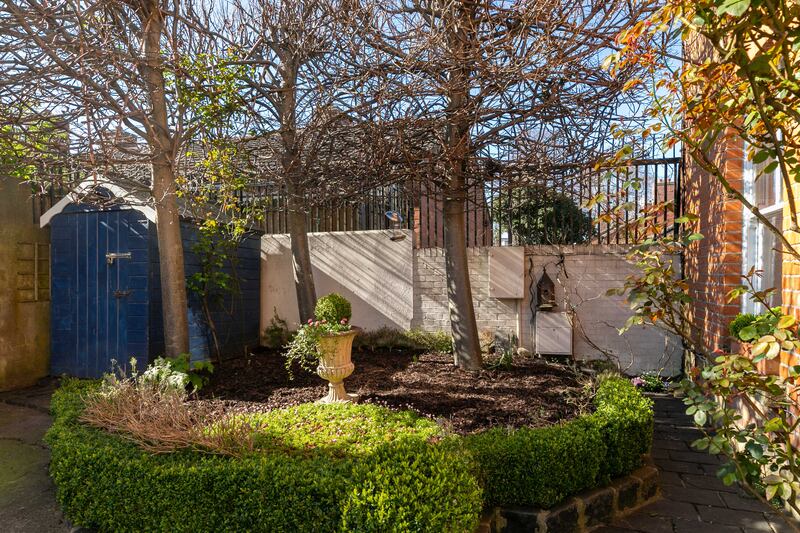 The house has a small front garden framed by mature lime trees and plenty of spring planting
