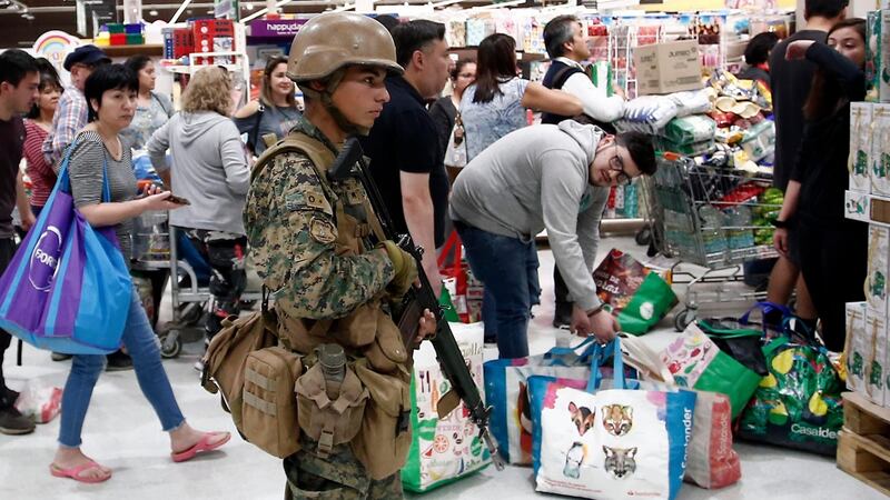 A military police stands guard at a supermarket as customers wait in line in Santiago, Chile. Photograph: Luis Hidalgo/AP