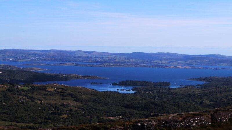 The land falls away steeply on either side, revealing an unrestricted view north to Kenmare Bay and The Magillicuddy Reeks.
