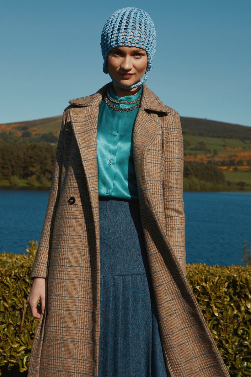 Aoife: Long-sleeved relaxed shirt in emerald blue, €285; textured wool pleated tailored skirt, €590; crochet bonnet in blue, €125; brown check tweed wrap coat, €695.