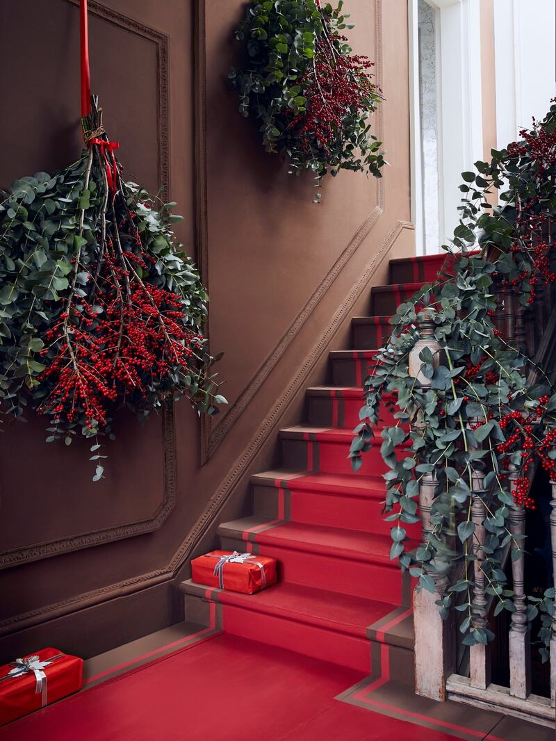 Annie Sloan’s festive hallway: Primer red on the  panelling and Emperor’s Silk painted as a runner on the floor. Large  willow wreaths are  wrapped in eucalyptus and hung with thick red ribbon while  red Hypericum berries drip down towards the floor.