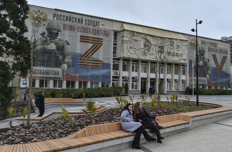 People sit on a bench in front of a building with a large banner in support of Russia's military campaign in Ukraine, in Yalta, Crimea, in May 2023. Photograph: EPA