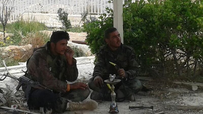 Two Syrian soldiers sit under an awning beside the church smoking a water pipe and ignoring a long burst of gunfire. Photograph: Michael Jansen