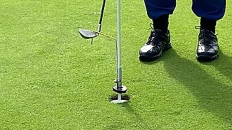 A golfer in France uses his club to remove the flagstick under new protocols.