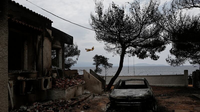 A firefighting airplane flies behind a burned house following a forest fire in Mati a northeast suburb of Athens, Greece, 24th of July, 2018. Photograph: YANNIS KOLESIDIS/EPA