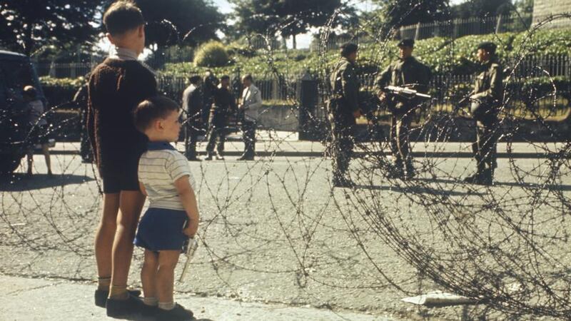 Two boys watch British soldiers on the Crumlin Road in Belfast through coils of barbed wire. Photograph: Rolls Press/Popperfoto/Getty