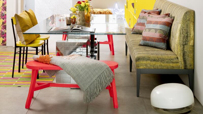 The kitchen is bright yellow and grey, strong patterned rugs abound, the dining plates are daffodil yellow and so are the bookshelves