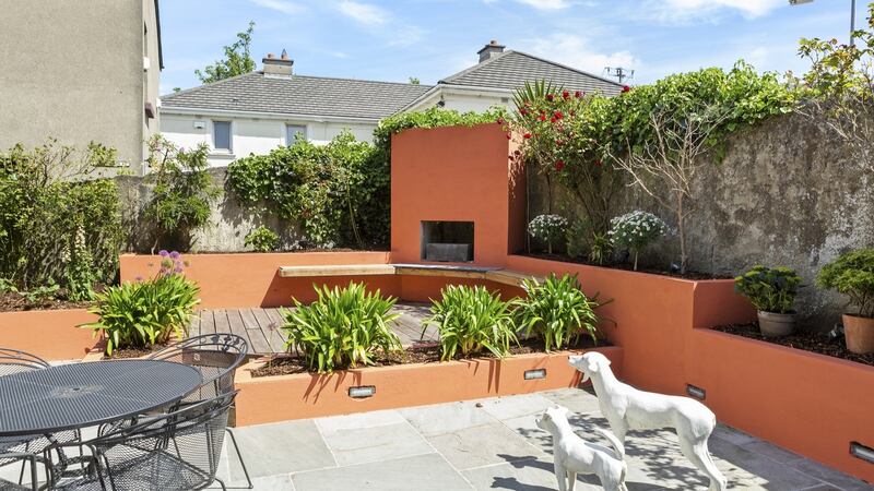 The south-facing garden, a contemporary space broken into different areas by low terracotta-painted walls, includes an outdoor fire with bench seating