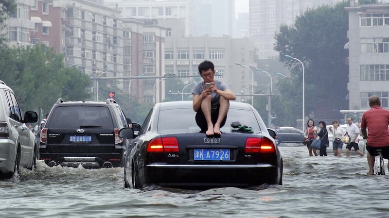 A man sits on top of a car as he is stranded on a flooded street in Tianjin, China. Photograph: Reuters