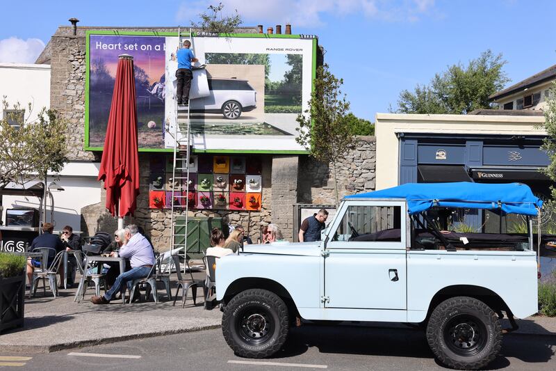 Replacing a Range Rover advert beside a parked 1960 Land Rover, in Dalkey during the Vintage Festival. Photograph: Dara Mac Dónaill