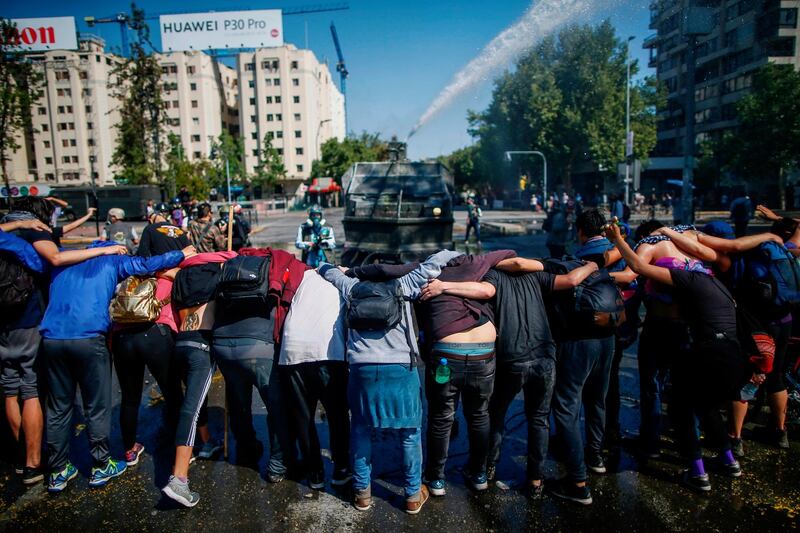 Demonstrators make a line as riot police repel with a water cannon during protests in Santiago on Sunday. Photograph: Pablo Vera/AFP/Getty