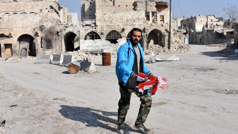 A Syrian pro-government forces soldier holds flags bearing the portrait of Syrian president Bashar al-Assad as he patrols Aleppo’s Bab al-Nairab neighbourhood on Saturday. Photograph: AFP/Getty Images