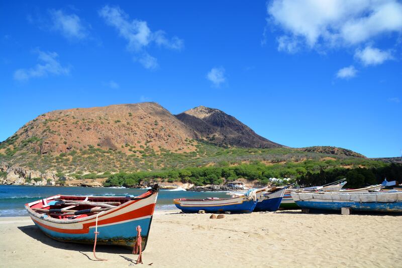 Tarrafal beach with white sand, clear water, coconut palms and colourful boats. 