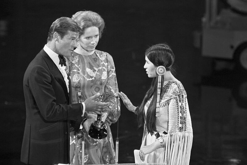 Roger Moore and Liv Ullmann, presenting the award, retreat back politely when Littlefeather reaches the stage and allow her to make a brief statement