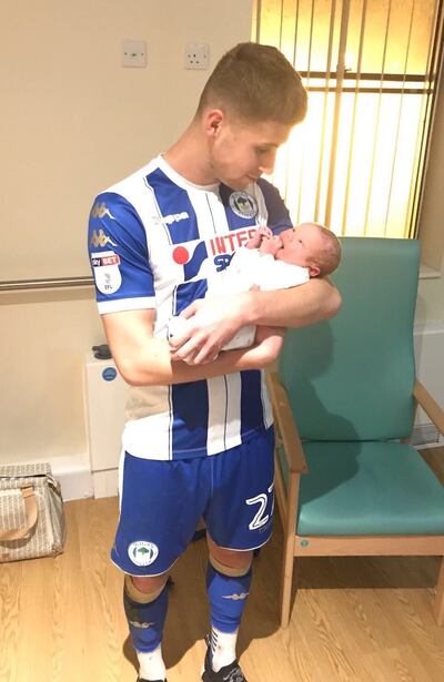 Ryan Colclough holds his newborn son Harvey Thomas while still wearing his full Wigan kit.